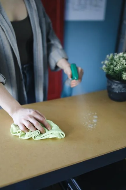 a-woman-in-a-green-shirt-and-black-gloves-vacuuming-a-gray-ottoman-5txz228u4eo